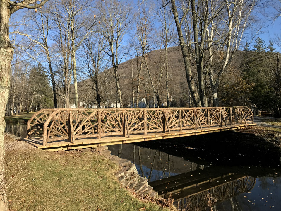 Historic recreation of a rustic bridge crossing a stream built using bark-on trees and branches at Kirkside Park in Roxbury NY