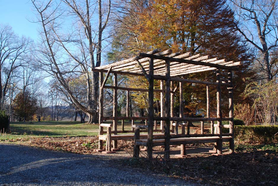 Outdoor rustic sitting shelter with built in benches constructed using bark-on trees and branches at Locust Grove