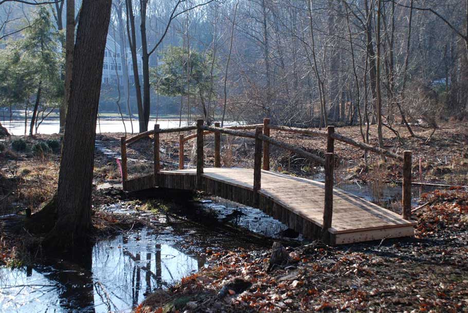 Rustic bridge custom built using cedar trees titled the Watershed Bridge