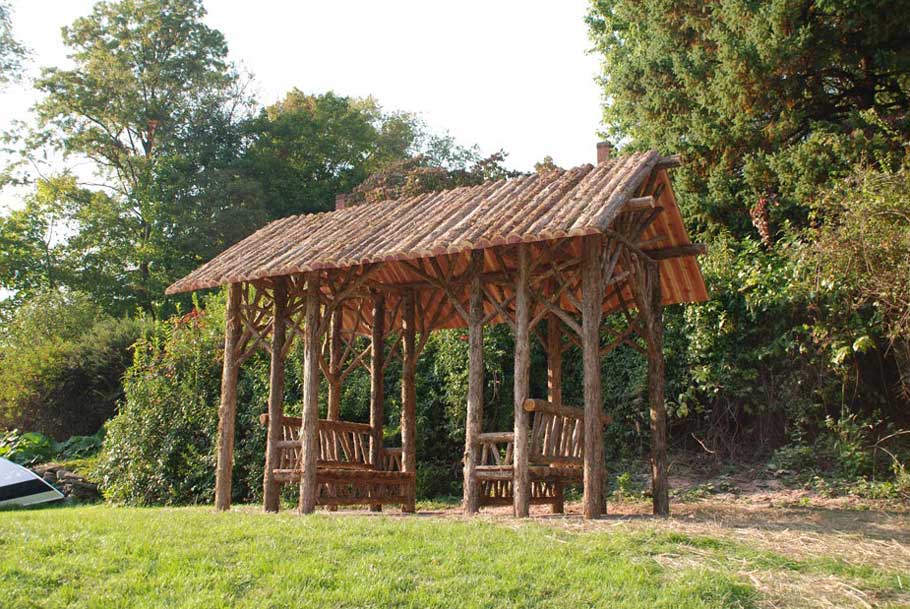 Outdoor sitting shelter built in the rustic style using logs and branches titled the Langer Shelter