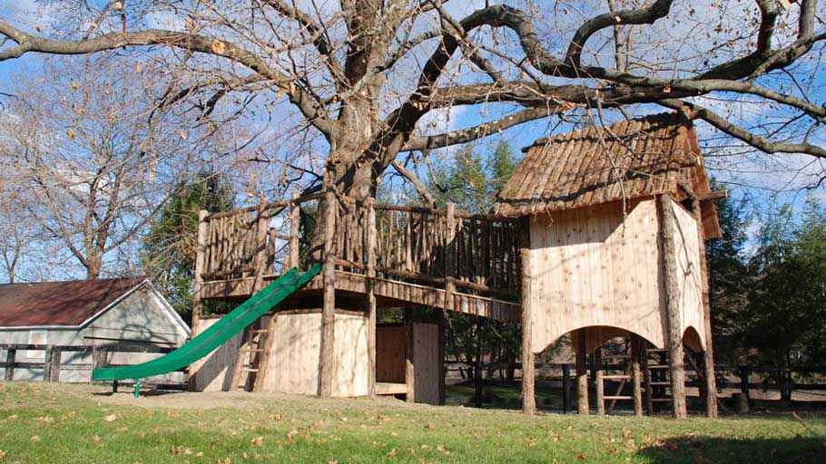 Outdoor cedar play structure built using bark-on trees and branches titled the Dewey Tree Fort